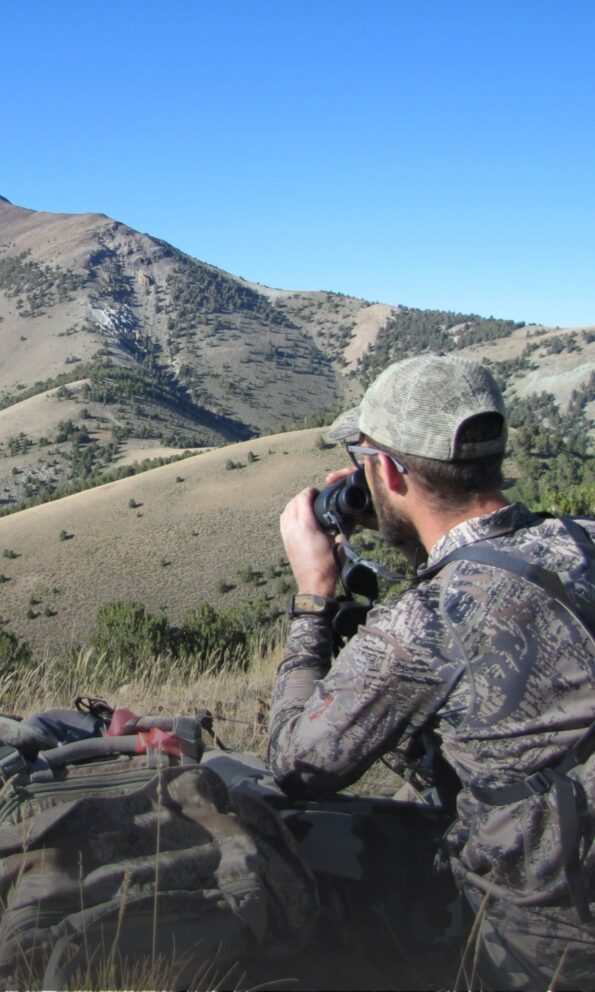 Hunter uses binoculars to look over mountain ridge