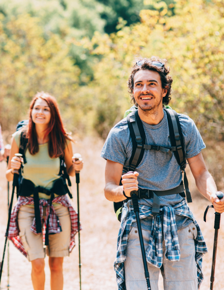 A man and woman hike with hiking poles and enjoy the scenery around them.